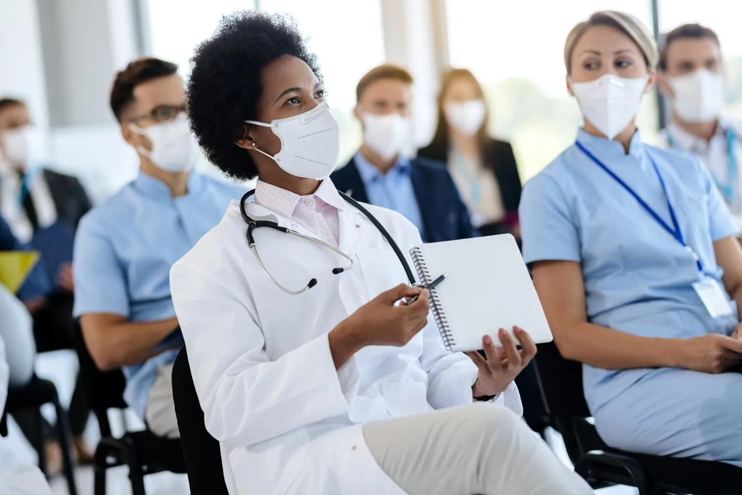 Health professionals wearing masks take notes during a briefing