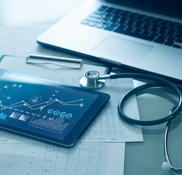 A tablet showing healthcare analytics charts beside a stethoscope and laptop