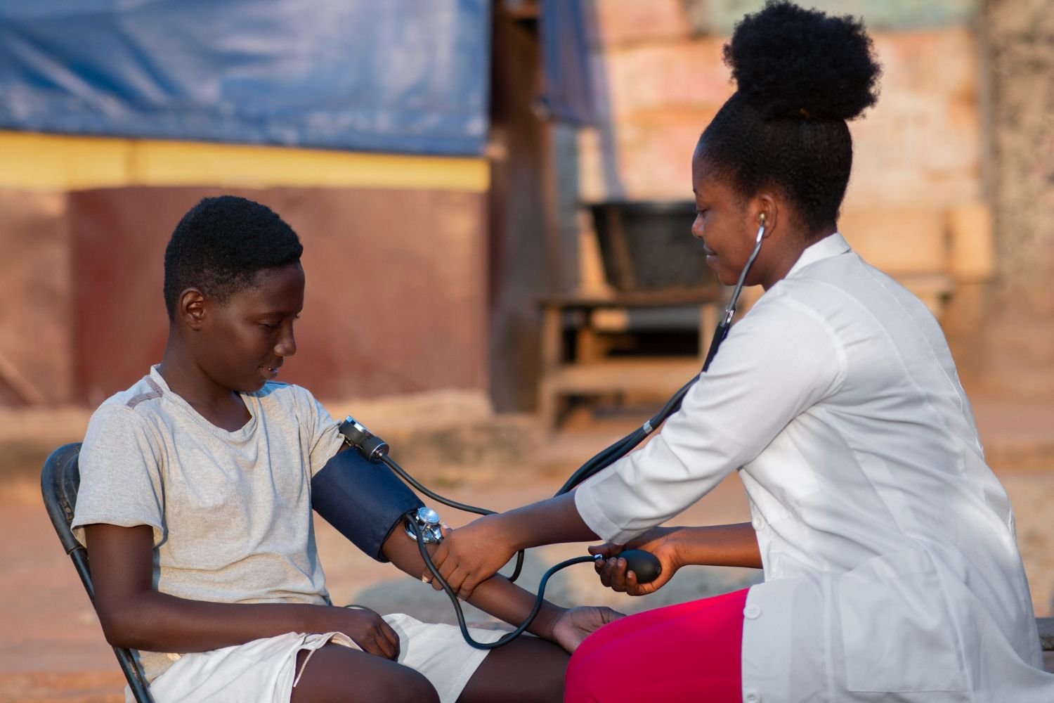 A health worker checks a young person's blood pressure outdoors in a community setting