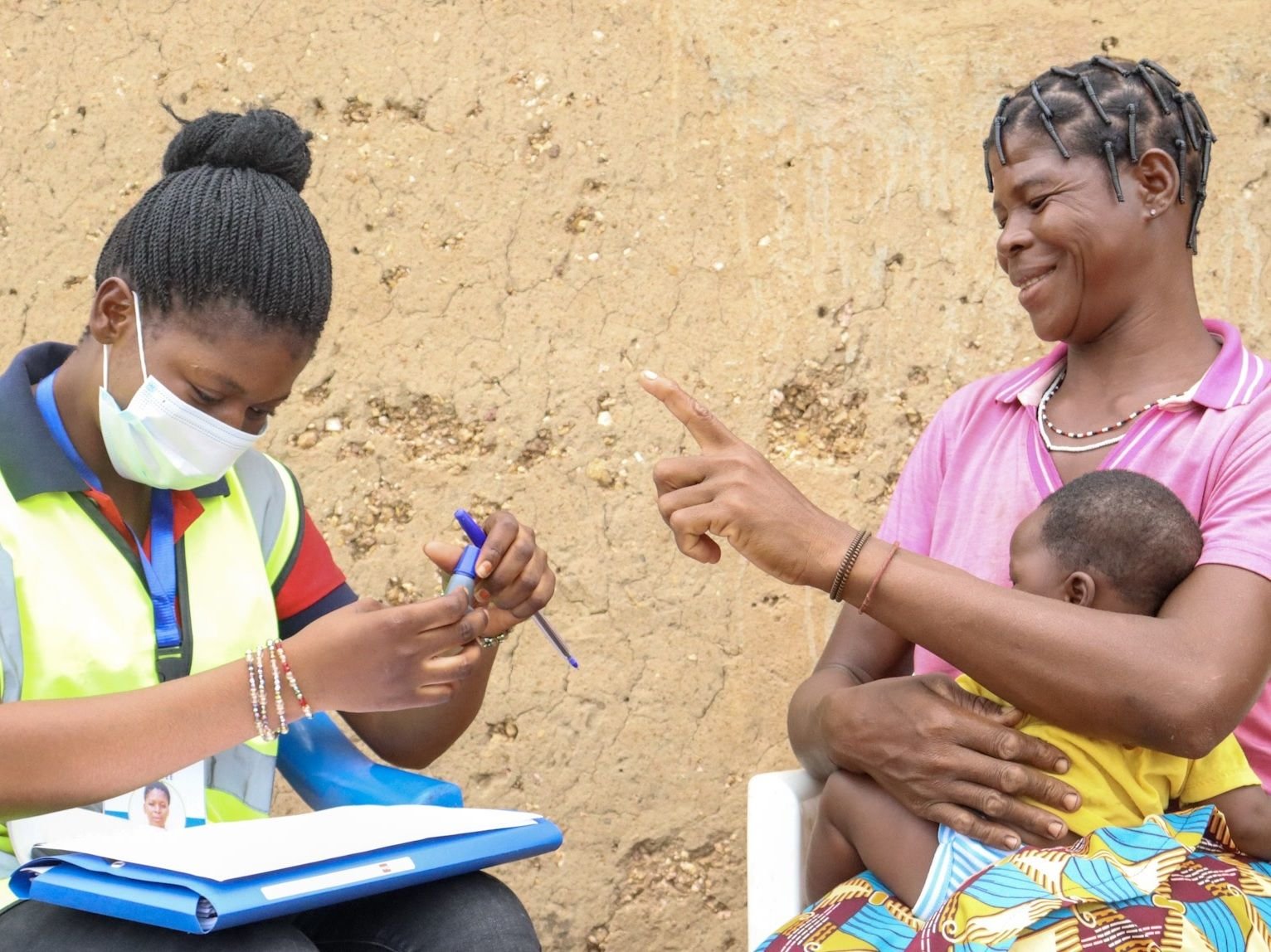 A community health worker records information while speaking with a mother holding her baby